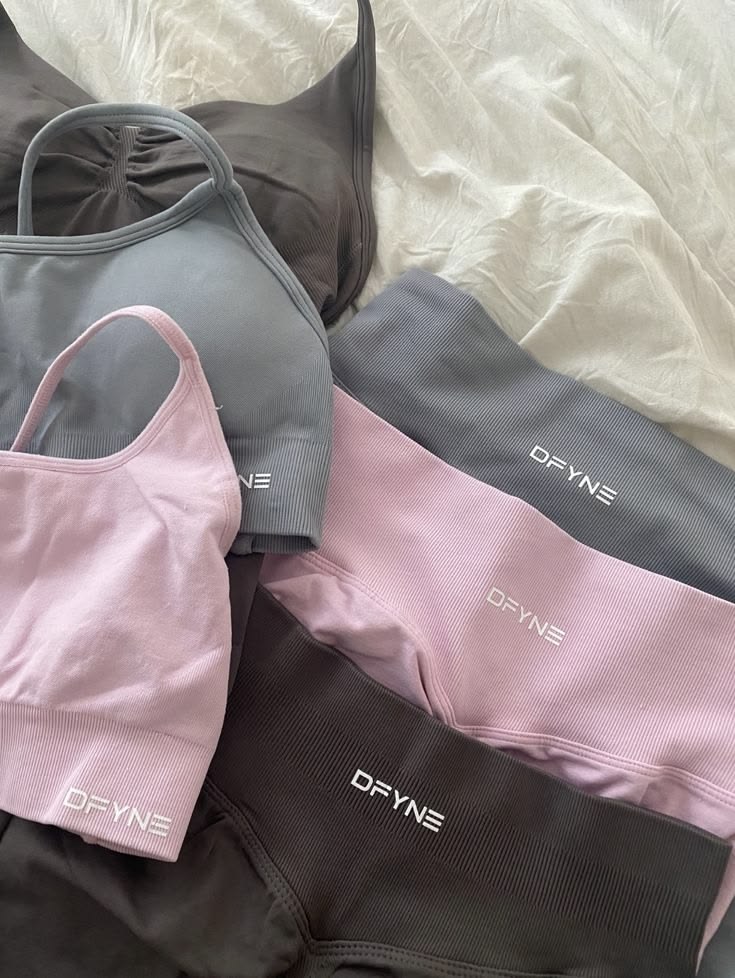 Assortissement de vêtement de sport de la marque Dfyne pliés et superposés sur un drap blanc.